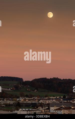 Der Vollmond steigt über die ländliche Landschaft bei Sonnenuntergang in der Schweiz auf. Stockfoto