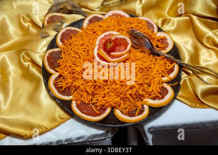 Geriebener Karottensalat mit Grapefruitscheiben und Kirschtomaten auf einem schwarzen Teller Stockfoto
