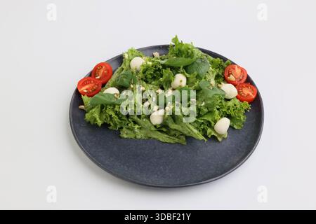 Sommerfrischer Diätsalat mit Kirschtomaten, Mozzarella, Basilikum und Olivenöl auf dunkler Platte auf weißem Hintergrund. Gesundes Mittagessen. Stockfoto