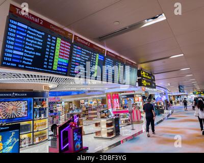 Abflugplätze zeigen Flüge am Terminal 2 an, während Reisende an Geschäften vorbeilaufen und die geschäftige Atmosphäre des Flughafens hervorheben. Stockfoto