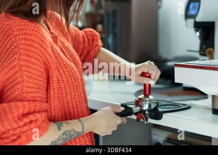 Schließen Sie die Hände der Frau mit einem Manipulationsschieber am Portafilter, um Espresso in der modernen Caféküche zuzubereiten. Stockfoto