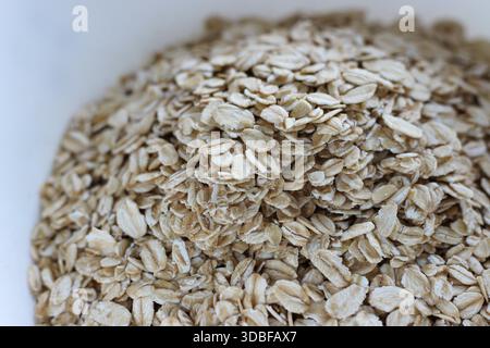 Haufen Haferflocken in einer Schüssel, Nahansicht. Haferflocken Textur, gesunde Frühstückszutat, neutraler Hintergrund Stockfoto