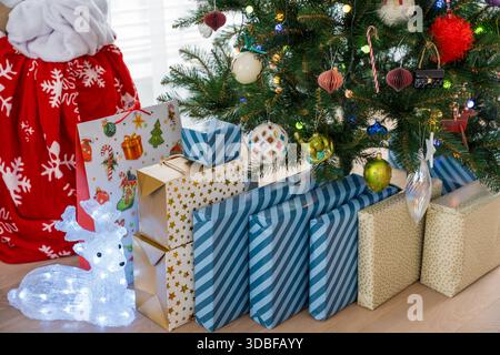 Eingewickelte Weihnachtsgeschenke unter künstlichem Kunststoff-Weihnachtsbaum im modernen Innenraum Stockfoto