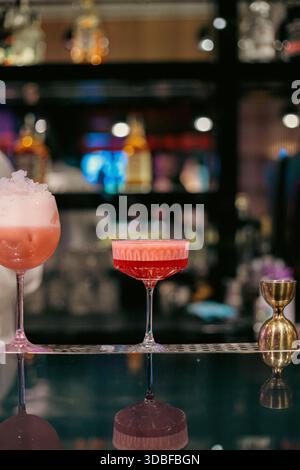 Stilvolle Nahaufnahme zweier roter Cocktails in Stielgläsern auf einer modernen Bartheke mit Schaum-, Zitrusgarnitur und stimmungsvoller Atmosphäre im Nachtleben Stockfoto