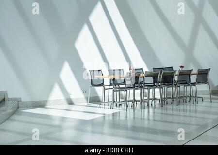 Minimalistisches Büro- oder Café-Interieur mit Stühlen, Tisch und dramatischen diagonalen Schatten vom Fenster. Stockfoto