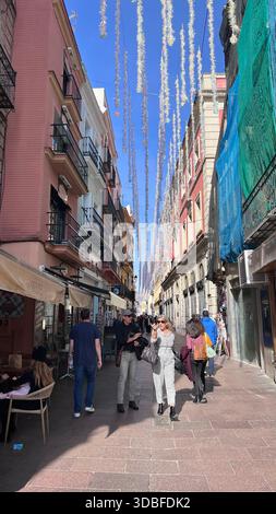 Festliche enge Straße in Sevilla, Spanien, mit hängenden Girlanden, farbenfrohen Fassaden, Balkonen und lebhaftem andalusischem Stadtcharme. Stockfoto