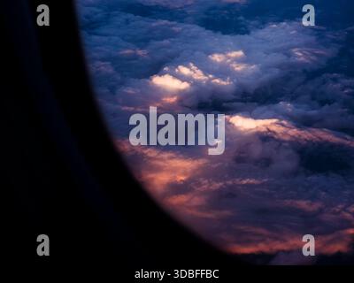 Das Flugzeugfenster zeigt einen dramatischen Dämmerhimmel mit warmen Sonnenlichtfarben, die eine riesige Decke aus flauschigen Cumulus-Wolken beleuchten und so eine friedliche und friedliche Atmosphäre schaffen Stockfoto