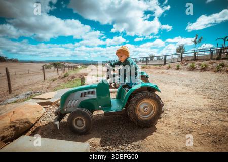 Ein Kind fährt gerne auf einem farbenfrohen Spielzeugtraktor auf einem wunderschönen Bauernhof Stockfoto