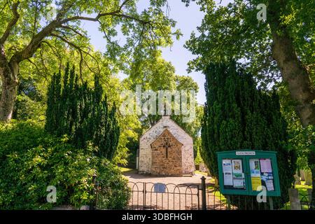 Bezaubernde Steinkapelle, eingerahmt von üppigen Nadelbäumen und Reifen Eichen, hinter einem schmiedeeisernen Tor mit einer gemeinschaftlichen Hinweistafel. Eine friedliche historische Stätte Stockfoto