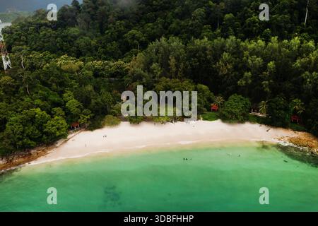 Türkisfarbenes Wasser hüllt sanft an ein sandiges Ufer, das von dichten grünen Hügeln umgeben ist. Diese ruhige Küstenszene fängt das Wesen eines tropischen Paras ein Stockfoto