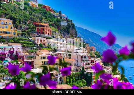 Atemberaubender Blick aus der Vogelperspektive auf die farbenfrohe Stadt Positano, die steil auf den grünen Hügel hinabsteigt und das glitzernde blaue Meer mit leuchtenden violetten Bougainvillea-Blumen besticht Stockfoto