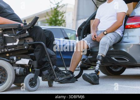 Zwei Freunde genießen die Zeit zusammen vor einem Auto, einer in einem Rollstuhl und der andere mit einer Beinprothese. Stockfoto