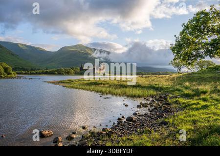 Dramatische Landschaft mit den historischen Ruinen von Kilchurn Castle neben Loch Awe, mit grünen Ufern, sanften Hügeln und einem bewölkten Himmel. Ein friedlicher SC Stockfoto