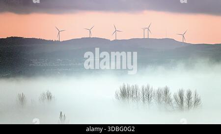 Glasgow, Schottland, Großbritannien. Dezember 2025. Wetter in Großbritannien: Niedriger Nebel, der auf einen plötzlichen Temperaturabfall über dem westlichen Ende der Stadt hinweist, sah, wie die Windfarm der Windmühlen südlich der Stadt ihre Anwesenheit bei Sonnenuntergang durch den absteigenden Nebel bekannt machte. Credit Gerard Ferry/Alamy Live News Stockfoto
