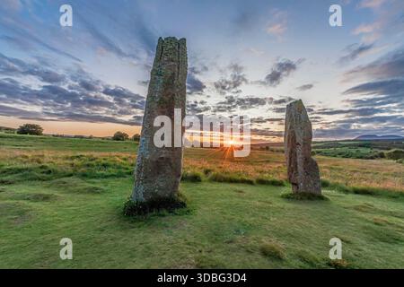 Zwei alte stehende Steine erheben sich aus einem üppigen grünen Feld, während die Sonne auf Machrie Moor, Schottland, untergeht. Eine beschauliche, zeitlose Szene, die an Tradition und Tradition erinnert Stockfoto