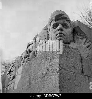 Schwarzweiß-Archivfoto, das eine dramatische Nahaufnahme des „Leninskaja Iskra“-Denkmals in Druschkiwka, Donezk-Region, Ukraine, Donbass, 1970er Jahre zeigt Das Basrelief aus Stein zeigt die entschlossenen Gesichter junger unterirdischer Kämpfer und eine Hand, die ein in rauen Granit gehauenes Faltblatt hält. Ein mächtiges Detail sowjetischer Monumentalkunst, das den antifaschistischen Widerstand des Zweiten Weltkriegs ehrt. Ein feierlicher Blick auf die historische Erinnerung in der friedlichen Stadt lange vor dem modernen Krieg. Stockfoto