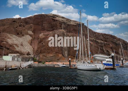 Weiße Segelboote legen an schwimmenden Docks unter rostfarbenen Klippen in Ponta de Sao Lourenco, Madeira, an. Weiches Nachmittagslicht und Wolken definieren die Schicht Stockfoto