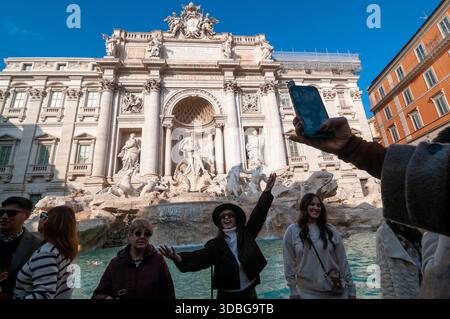 Ein Touristenmädchen mit Hut posiert vor dem Trevi-Brunnen für ein Smartphone-Foto in Rom. Stockfoto