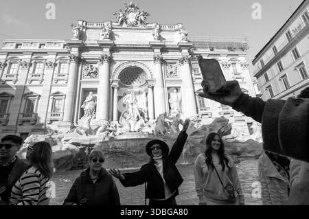 Ein Touristenmädchen mit Hut posiert vor dem Trevi-Brunnen für ein Smartphone-Foto in Rom. Stockfoto