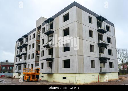 Modernes, vorgefertigtes Betonwohngebäude im Bau mit unfertigen Fenstern, temporären Balkonen und Baugeräten Stockfoto
