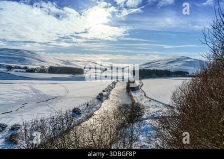 Schneebedeckte Felder und ein glitzernder Fluss in einem ruhigen Yarrow-Tal unter einem klaren blauen Himmel. Stockfoto