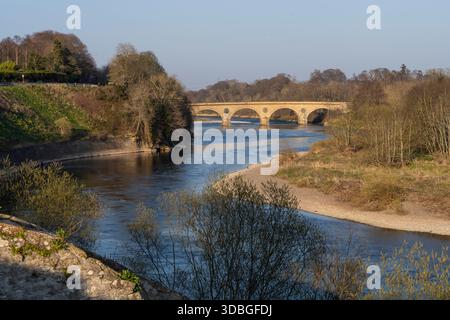 Ruhiger Fluss fließt unter einer historischen Steinbrücke in einer ruhigen englischen Landschaft. Stockfoto