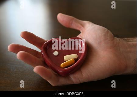 Nahaufnahme einer menschlichen Hand, die einen rosafarbenen herzförmigen Pillenbehälter mit Kapseln und Tabletten auf hölzernem Hintergrund hält. Konzeptbild für Heilung Stockfoto