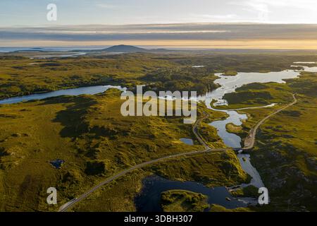 Luftaufnahme des sich windenden Flusses durch das grüne Moorland bei Sonnenuntergang über der fernen Insel, Galway, irland Stockfoto