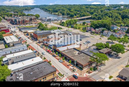 Blick aus der Vogelperspektive auf die Innenstadt von Algonquin Illinois entlang des Fox River mit Straßenlandschaften am Flussufer, Brückenüberquerung, Yachthafen und lokalen Unternehmen. Stockfoto