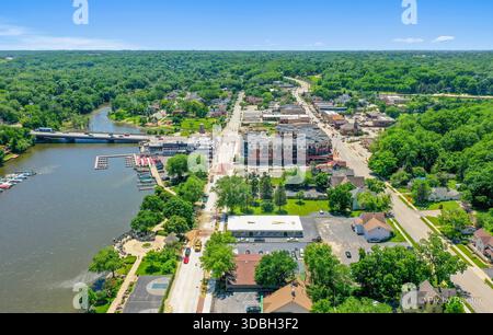 Blick aus der Vogelperspektive auf die Innenstadt von Algonquin Illinois entlang des Fox River mit Straßenlandschaften am Flussufer, Brückenüberquerung, Yachthafen und lokalen Unternehmen. Stockfoto