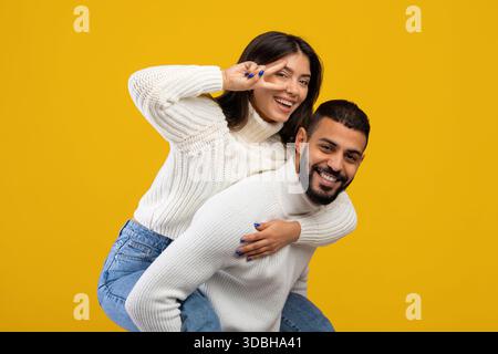 Ein Paar, das Spaß mit verspielten Posen vor einem leuchtend gelben Hintergrund hat Stockfoto