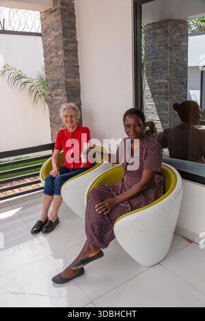 Lilongwe Malawi Afrika. 12.11.2025. Schwarzafrikanische Pflegeperson sitzt mit älteren Weißen in Lilongwe Malawi. Stockfoto