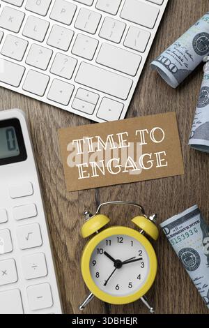 Karte mit Textzeit zum Einschalten, Wecker, Dollar, Taschenrechner und Computertastatur auf Holztisch. Flache Lagen Stockfoto