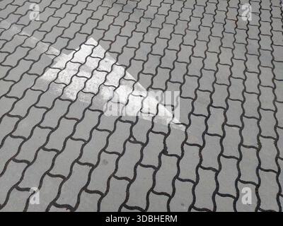 Eine Straßenmarkierung zeigt einen Pfeil auf dem Bürgersteig in einer Stadt. Das steinähnliche Muster des Gehwegs ist zusammen mit der durch das A angegebenen Richtung sichtbar Stockfoto