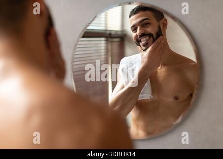 Selbstbewusster junger arabischer Mann, der morgens die Hautpflege-Routine im modernen Badezimmer genießt Stockfoto