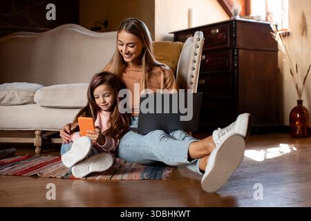 Mutter und Tochter genießen eine gute gemeinsame Zeit zu Hause, während sie Telefon und Laptop verwenden Stockfoto