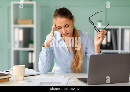 Junge Geschäftsfrau fühlt sich am Arbeitsplatz überfordert und gestresst, wenn sie an einem Laptop arbeitet Stockfoto