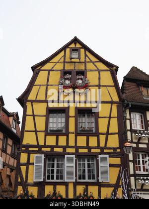 Colmar, Frankreich - 1. Dezember 2025: Buntes gelbes Fachwerkgebäude mit dunklen Holzbalken und weißen Fensterläden Stockfoto