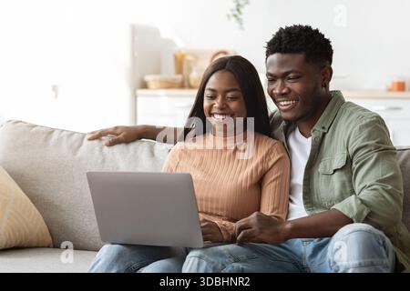 Junges Paar genießt ein gemütliches Wochenende zu Hause, während es Laptop zum Einkaufen und Surfen benutzt Stockfoto