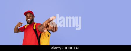 Mann in rotem Hemd und Kappe lächelt, während er auf blauen Hintergrund zeigt Stockfoto