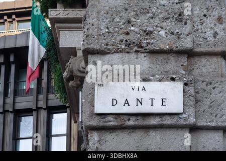 VIA DANTE - Schild einer Einkaufsstraße in Mailand, eine Steinmauer mit italienischer Flagge. Stockfoto