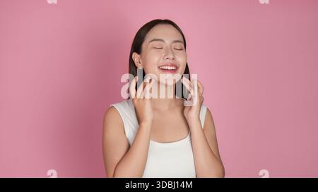 Frauen und Hautpflege Beauty. Fröhliche Frau, die Hautpflegeroutine mit geschlossenen Augen auf rosa Hintergrund genießt. Stockfoto
