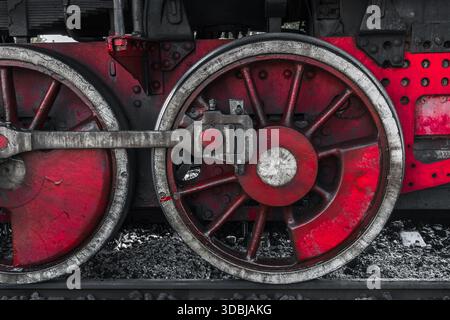Eine detaillierte Ansicht eines roten Dampflokomotivradsatzes mit verwittertem Metall, Speichen und einer Pleuelstange. Das Bild erinnert an Industriegeschichte, Macht Stockfoto