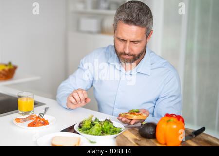 Der Mann frühstückt morgens in der Küche. Hispanischer Mann genießt eine gesunde Mahlzeit am Küchentisch. Ein Mann isst Getreide und Obst in der Küche Stockfoto