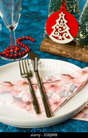 Entworfener eleganter Weihnachtstisch auf blauem Hintergrund mit leerem Teller, weihnachtsschmuck und Sektgläsern Stockfoto