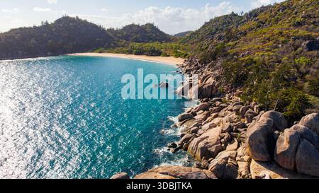 Blick aus der Vogelperspektive auf das türkisfarbene Wasser trifft auf die zerklüftete, felsige Küste, gesäumt von der üppigen, grünen Vegetation von Magnetic Island, Queensland, Australien. Stockfoto