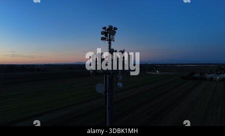 Mobilfunkturm steht vor dem dunkelblauen Himmel, ausgestattet mit verschiedenen Antennen für drahtlose Kommunikation und Mobilfunkdienste im gesamten Po Val Stockfoto