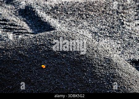 Eine kontrastreiche Nahaufnahme eines Hügels aus grobem, dunklem, körnigem Material – möglicherweise Schlacke, Kohle oder vulkanischer Asche – mit intensiver dunkler Textur. Ein Singen Stockfoto