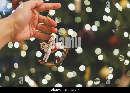 weihnachtsspielzeug mit Pferd in der Hand gegen festliche Weihnachtsbaumbeleuchtung. Symbol 2026. Frohes neues Jahr und frohes fest! ! Kopierbereich. Stilvolles Vintage-Ornament Stockfoto