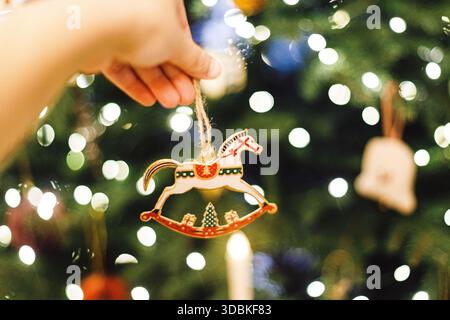 weihnachtsspielzeug mit Pferd in der Hand gegen festliche Weihnachtsbaumbeleuchtung. Symbol 2026. Frohes neues Jahr und frohes fest! ! Kopierbereich. Stilvolles Vintage-Ornament Stockfoto